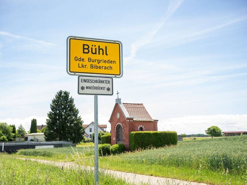 Ortsschild von Bühl mit kleiner Kapelle im Hintergrund